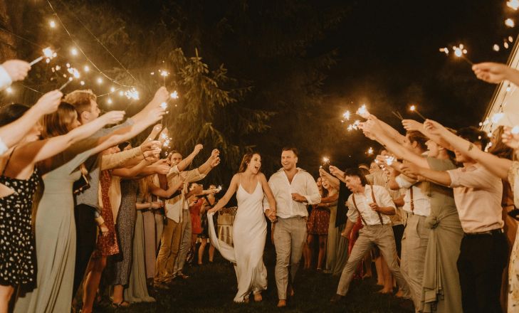 Bride and groom joyfully exit surrounded by sparkling celebratory guests at a nighttime wedding.
